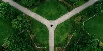 Unlocking Potential: Expert Strategies in Finance, Benefits, and Education Aerial view of a person at the convergence of three geometric pathways in a vibrant green urban park, symbolizing integrated strategies for finance, benefits, and education.