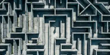 Unmasking Common Pitfalls in Finance, Benefits, and Education Strategies An aerial drone view of a person lost in a complex concrete labyrinth under harsh midday sun, symbolizing financial missteps and the illusion of quick wins.